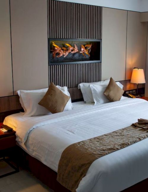 A neatly arranged hotel room features a large bed with pillows, lamps on side tables, and artwork on the wall, creating a cozy atmosphere.