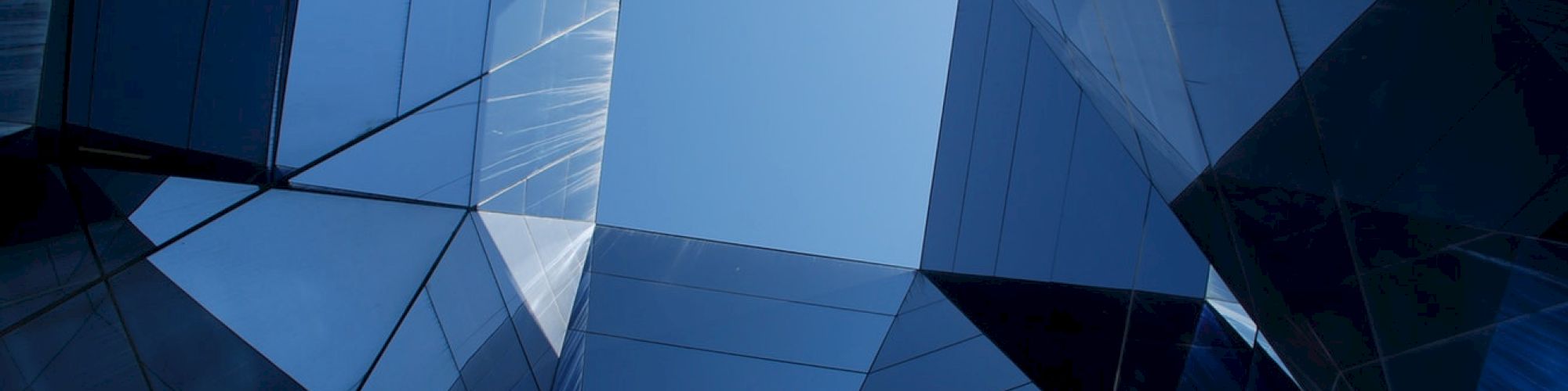 The image shows a geometric, glass and metal structure with a central opening to the sky, creating a modern architectural effect.