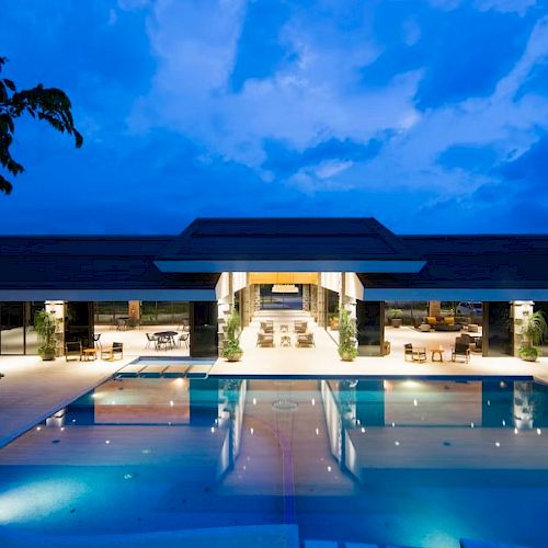 A luxurious building with a sleek, modern design is illuminated at night. It features a large pool reflecting the lights and clear sky.