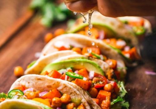 A hand squeezing lime over tacos filled with chickpeas, avocado, and vegetables on a wooden board.