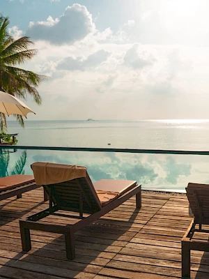 Poolside deck with sun loungers, umbrellas, and a view of the ocean under a cloudy sky.