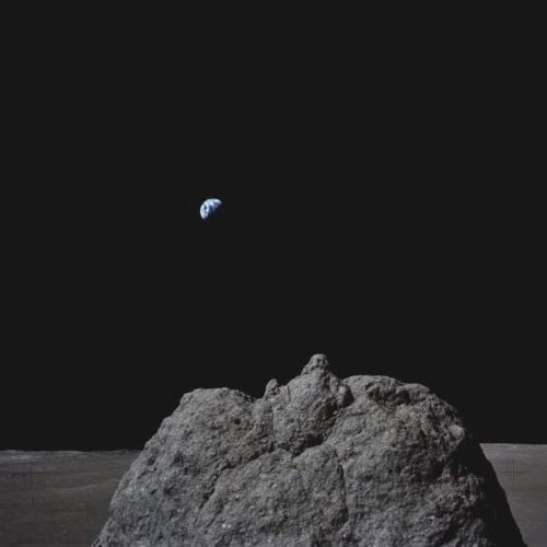 A lunar surface with a rock in the foreground and Earth visible in the dark sky.