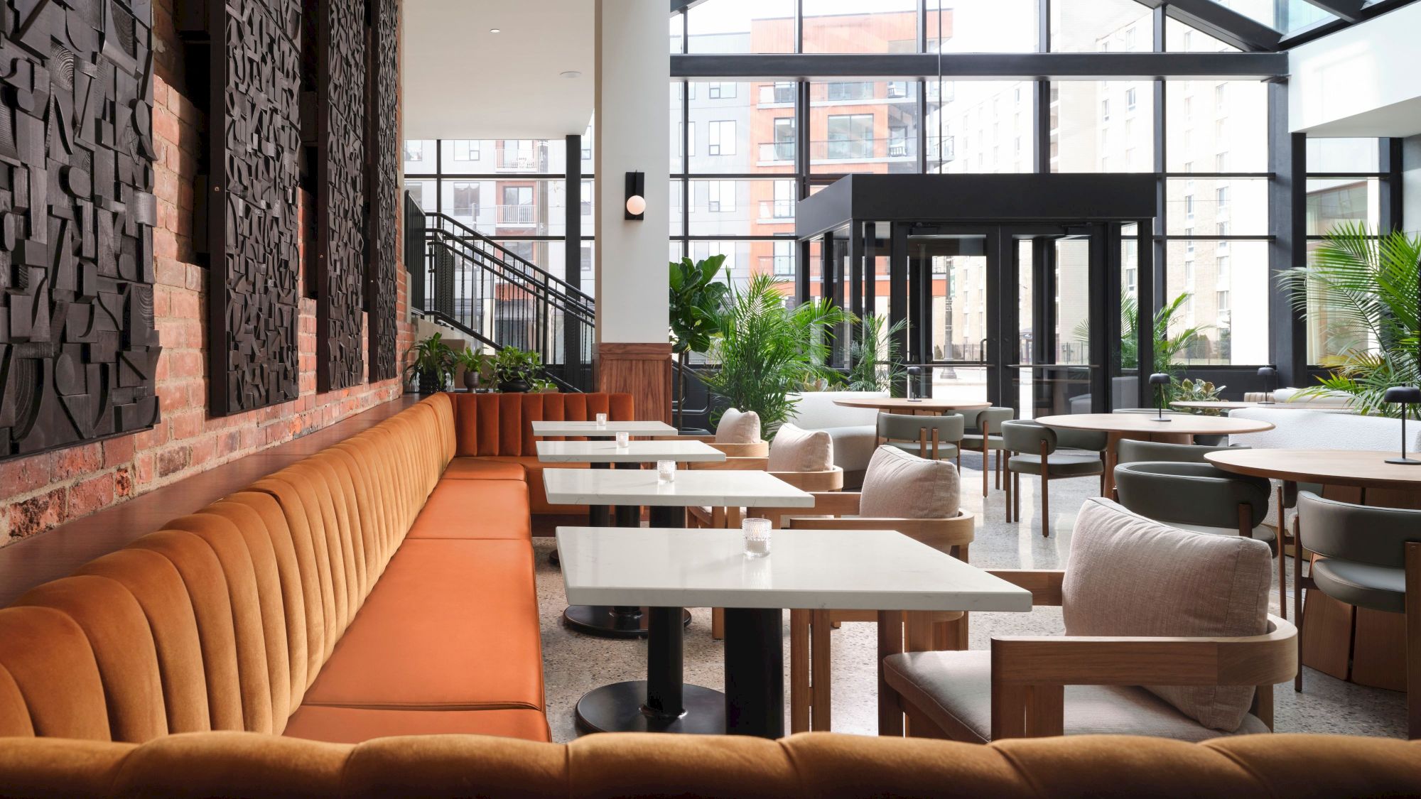 The image shows a modern, stylish restaurant with orange banquettes, white tables, and large windows allowing natural light to fill the space.