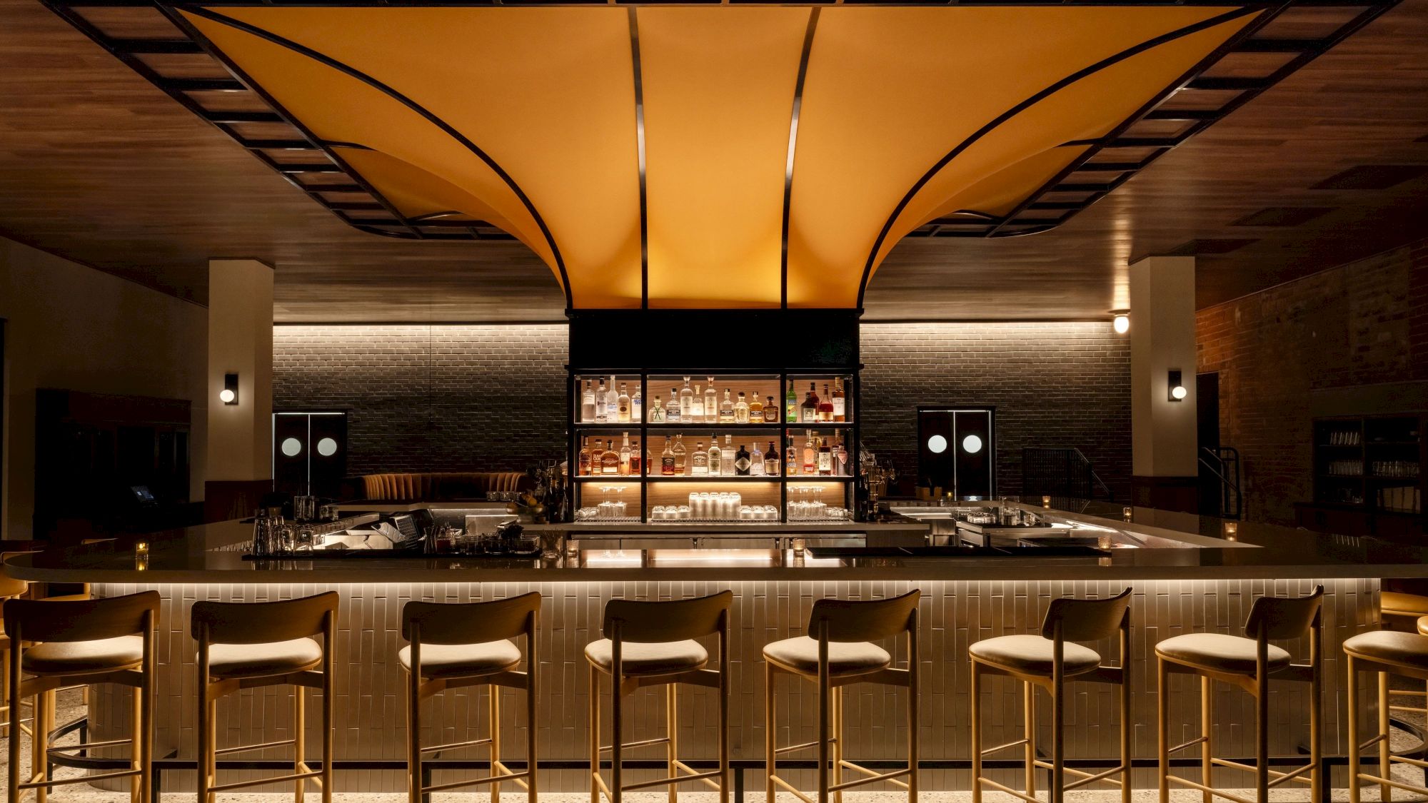 The image shows a modern, stylish bar with high chairs, ambient lighting, and a canopy ceiling, creating a cozy atmosphere.