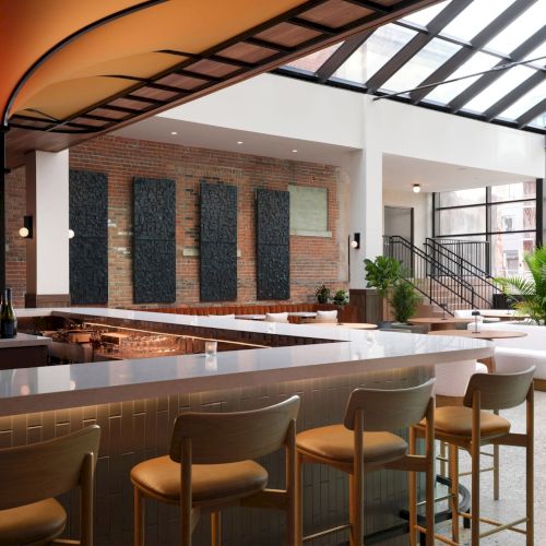 The image shows a modern, stylish bar with seating, a large skylight, and contemporary decor, creating a welcoming atmosphere.