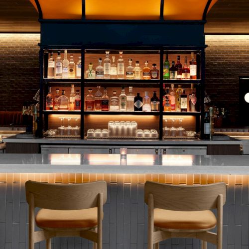 A stylish, modern bar with a central illuminated island, high-backed chairs, shelves with bottles, and warm lighting creating an inviting ambiance.