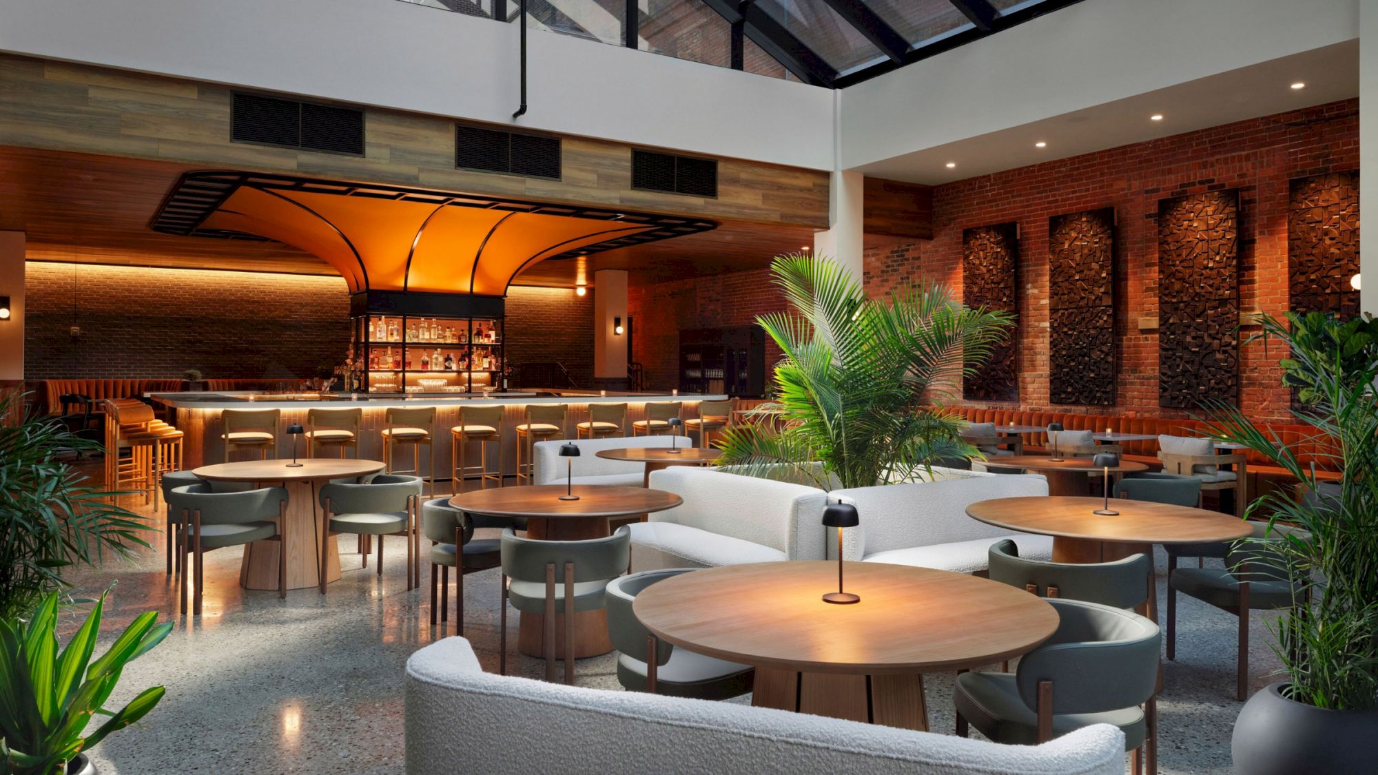 The image shows a modern, stylish restaurant with wooden tables, chairs, a bar area, and indoor plants, creating a cozy and inviting atmosphere.