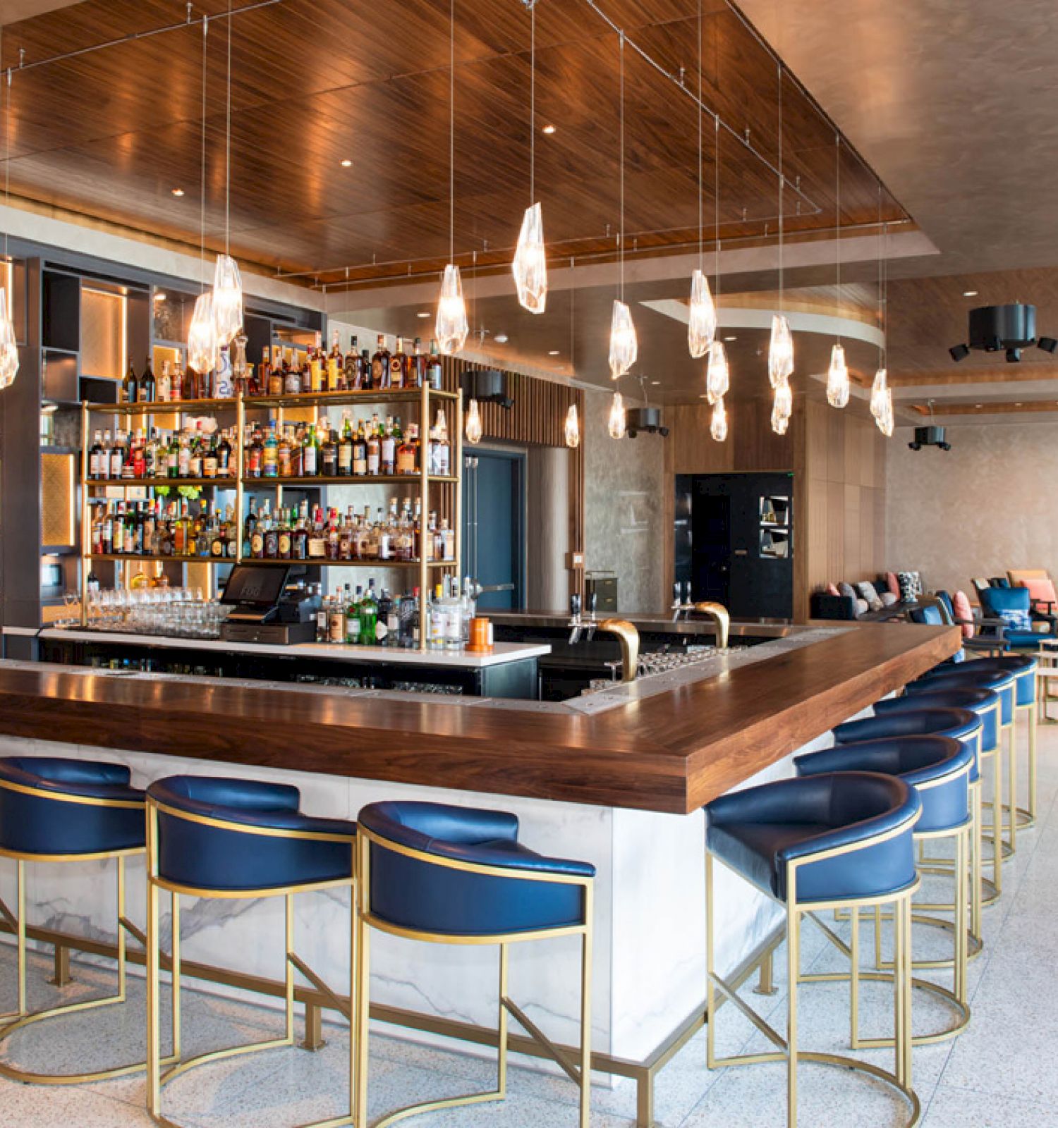 The image shows a modern bar interior with stylish lighting, a stocked bar area, and seating around the bar in a sophisticated setting.