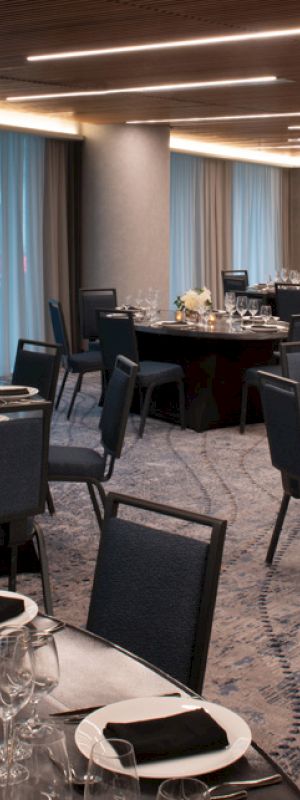 The image shows an elegantly set banquet room with round tables, chairs, and place settings prepared for a formal event or dinner.