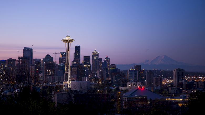 Seattle skyline at dusk, featuring the Space Needle and Mount Rainier in the background beneath a soft evening sky.