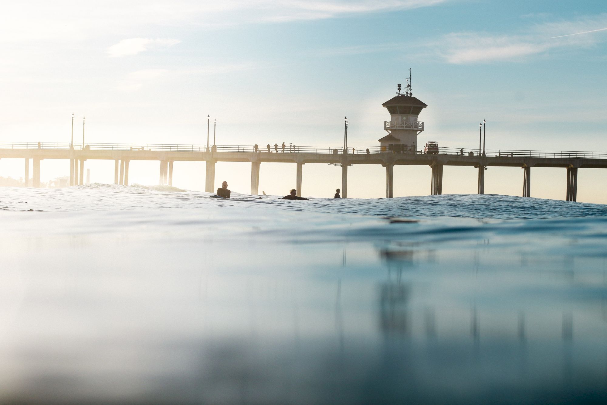 A pier extends over a calm ocean with people walking on it, under a blue sky.
